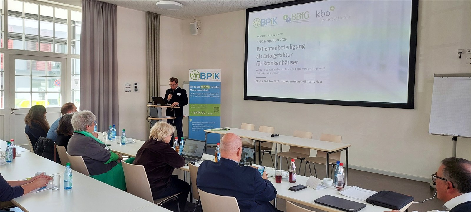 Nicolas von Oppen eröffnet das BPiK-Symposium am Rednerpult, auf der Leinwand die Titelfolie